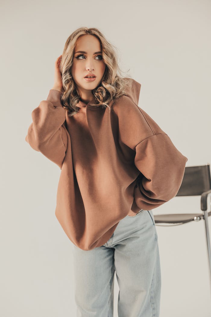 Stylish woman in oversized hoodie and jeans posing elegantly indoors.
