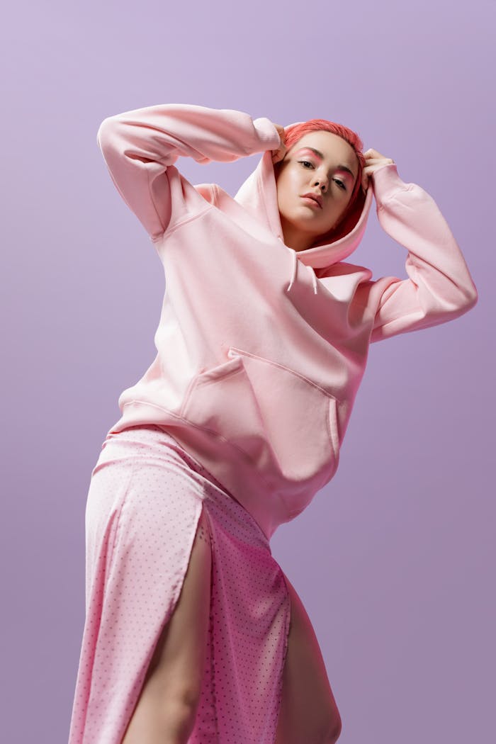 Fashionable woman in pink hoodie and skirt against a violet backdrop.